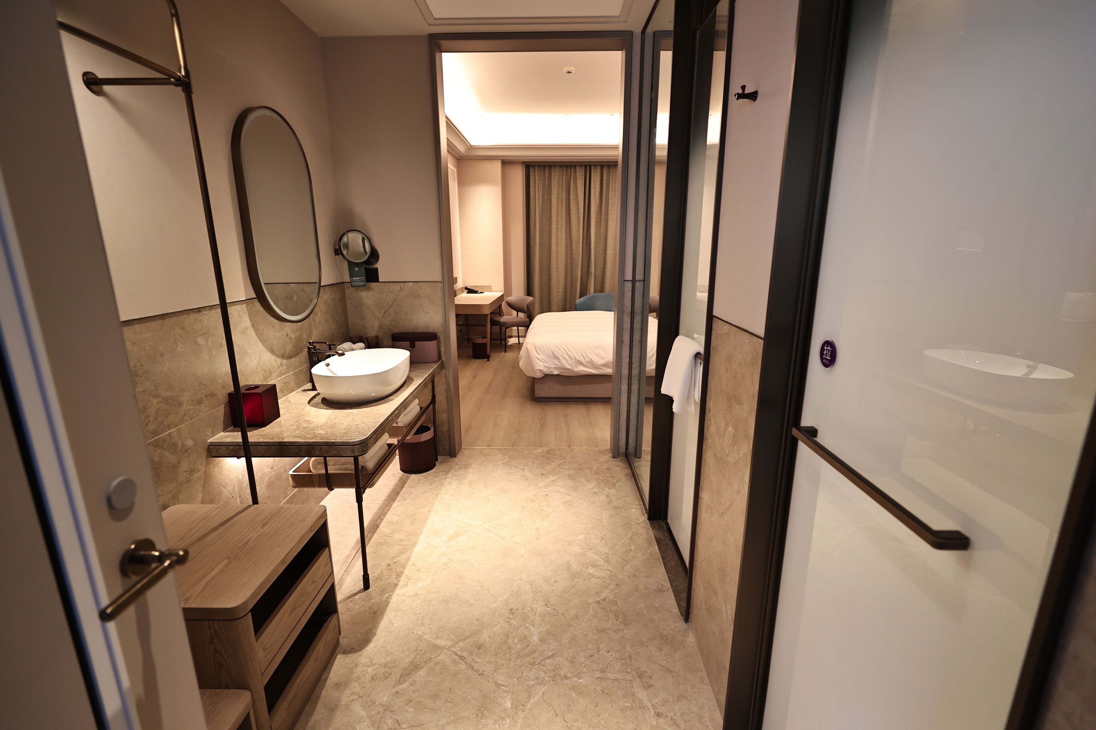 A hotel room with a bathroom, a bed, a desk, and a mirror.
