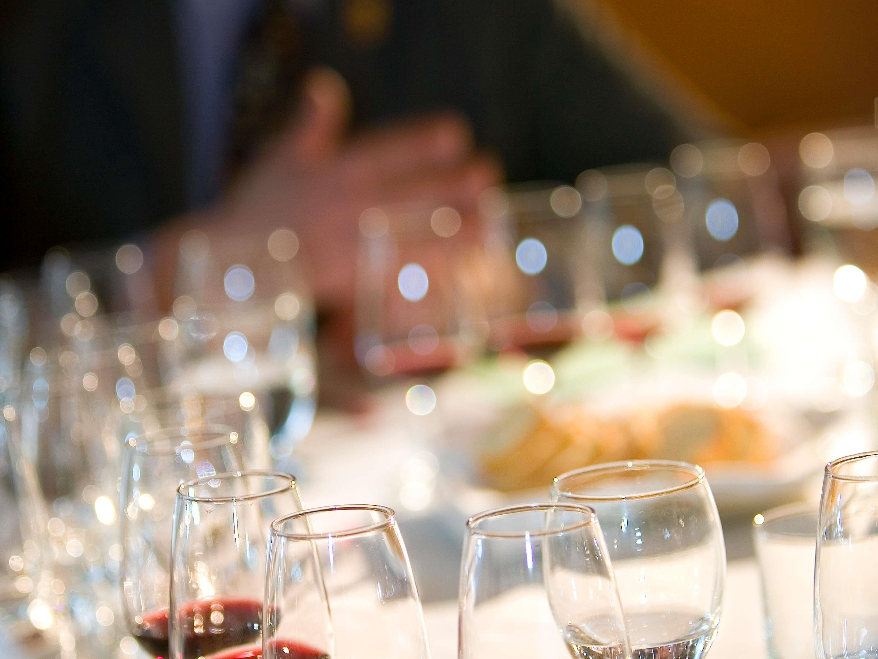 Una mesa con varios vasos, algunos llenos de un líquido rojo, probablemente vino, y otros vacíos.