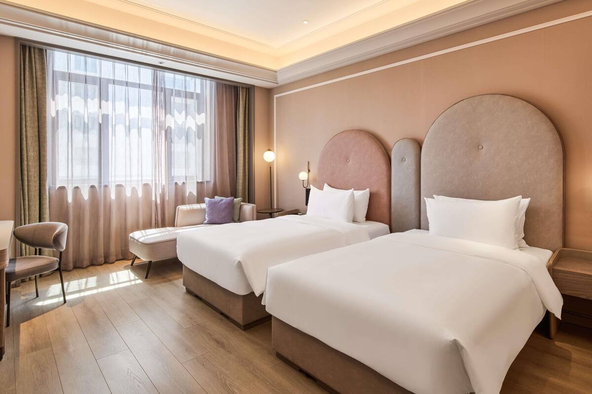 Une chambre d’hôtel avec deux lits, un bureau, une chaise et une grande fenêtre avec des rideaux.