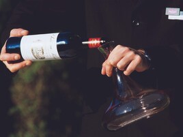 A person holding a wine bottle and pouring it into a decanter.