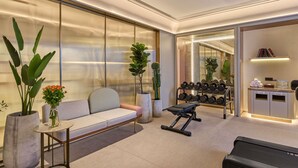 Une chambre d’hôtel moderne équipée d’un canapé, d’appareils de musculation, d’un tapis de course et d’un bureau avec tout le nécessaire.