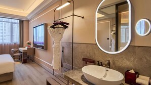 Ein Hotelzimmer mit Bett, Schreibtisch, großem Spiegel, Badezimmer mit Waschbecken und Duschbereich.