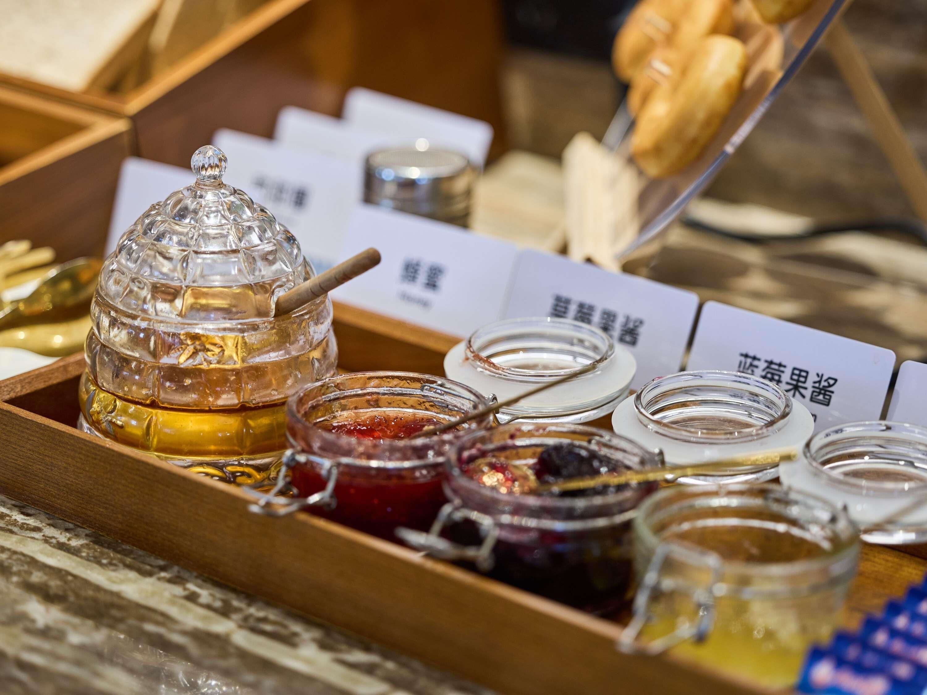 A tray with jars of honey and jams, a honey dipper, and a honey jar with a lid.