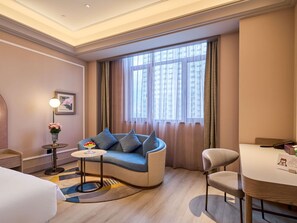 Ein Hotelzimmer mit einer Couch, einem kleinen runden Tisch, einem Sessel, einer Lampe und einem fenster mit Vorhängen.