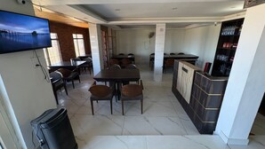 A restaurant with a TV on the wall, multiple tables and chairs, a trash bin, and a counter with shelves. - In The Beer Castle (Kufri)