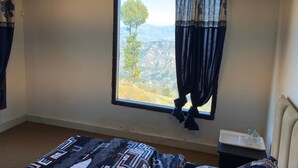 A bedroom with a large window, a bed, and a nightstand. - In The Beer Castle (Kufri)