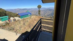 A balcony with a view of a mountainous landscape, a covered area with people, and a small tree. - In The Beer Castle (Kufri)