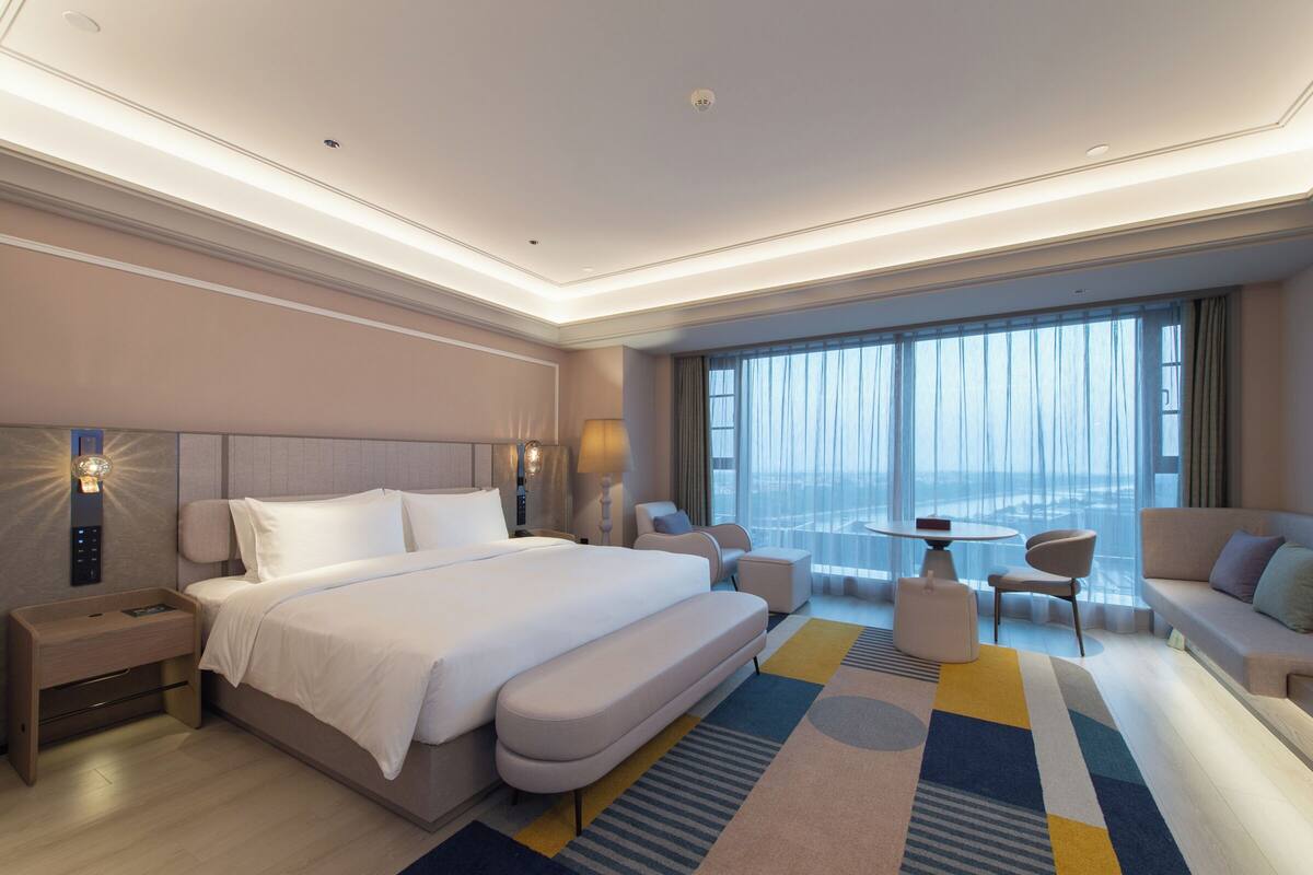 Habitación de hotel moderna con una cama grande, un sofá, una mesita y vistas a la ciudad.