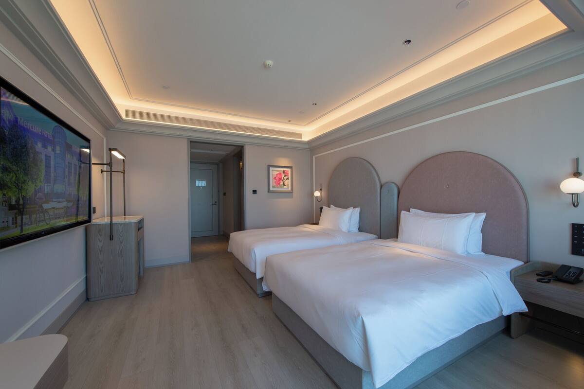Habitación de hotel con dos camas, un televisor de pantalla plana grande, una mesita de noche con teléfono y un cuadro en la pared.