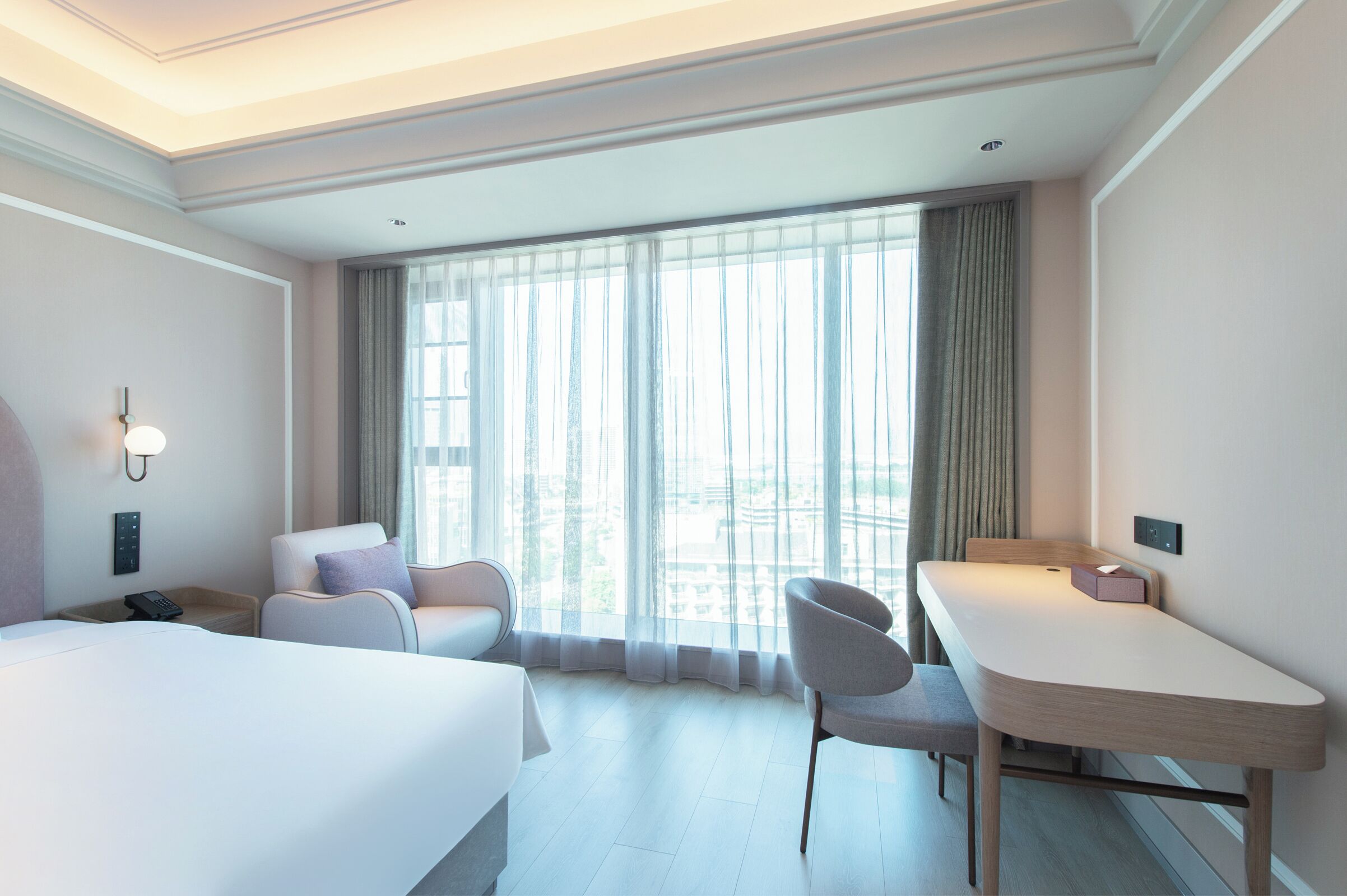 Een hotelkamer met een bed, een bureau, een stoel, een telefoon en een raam met gordijnen.