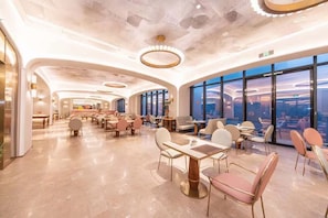 Un amplio vestíbulo de hotel con techos altos, candelabros modernos y grandes ventanales con vistas a la ciudad.