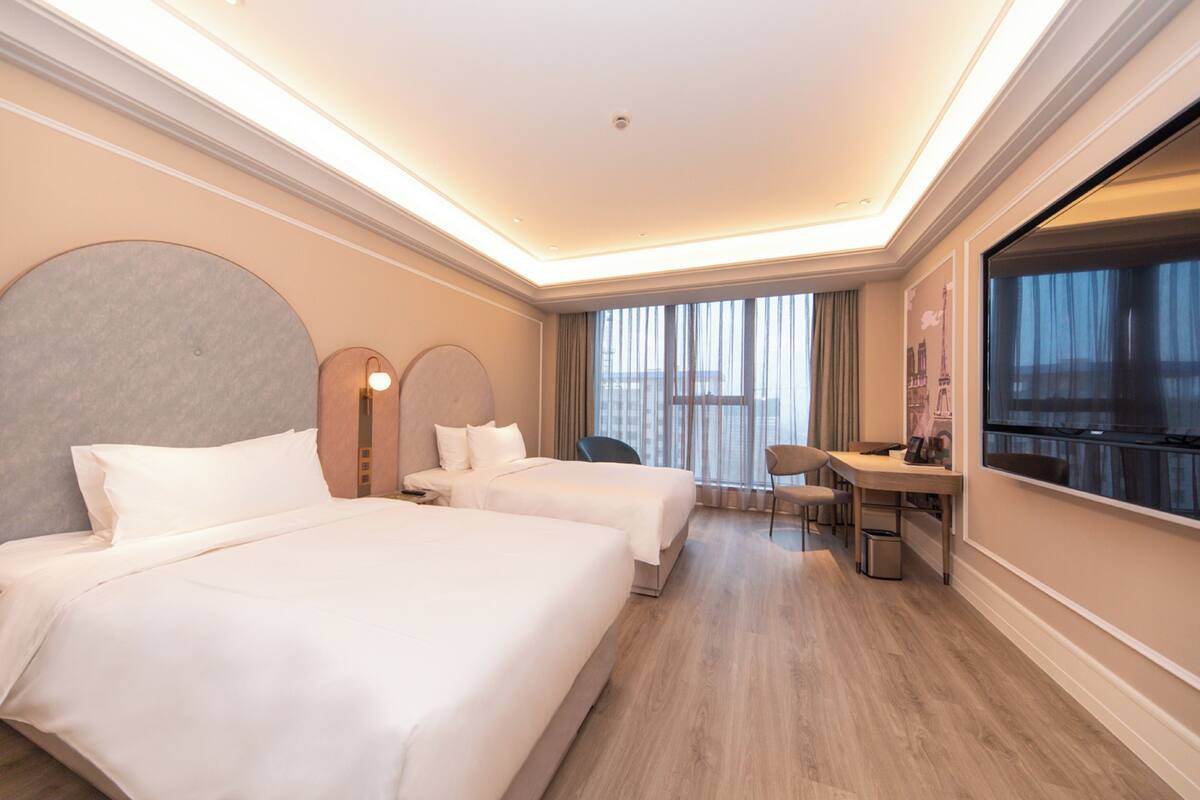 Een hotelkamer met twee bedden, een bureau, een stoel en een groot raam.