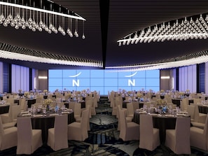 Un salón de banquetes con mesas redondas, sillas y un logotipo iluminado de gran tamaño en la pared de fondo.