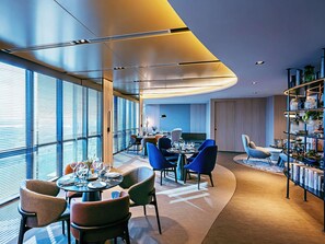 A modern dining area with round tables, chairs, and a bookshelf with books. - Novotel Johor Bahru City Centre (Johor Bahru)