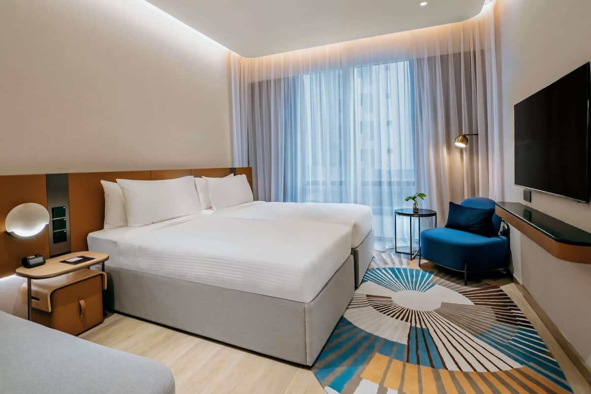 Una camera d'albergo moderna con un letto grande, una scrivania, una sedia, una televisione e una finestra con tende leggere.