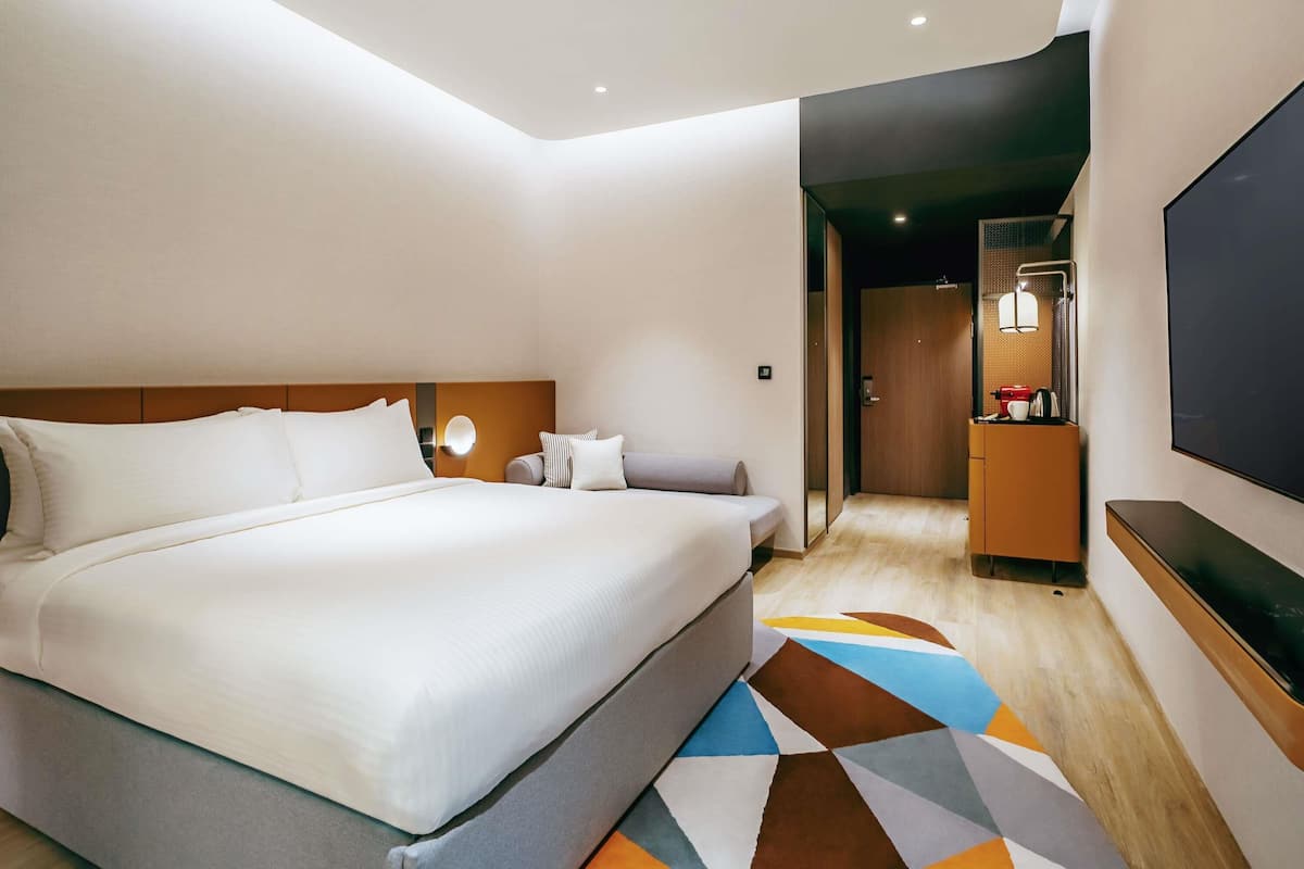Una habitación de hotel moderna con una cama grande, un sofá, un televisor de pantalla plana y una kitchenette pequeña.
