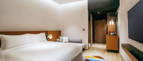A modern hotel room with a large bed, a sofa, a flat-screen TV, and a small kitchenette.