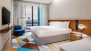 Habitación de hotel con una cama grande, televisión, escritorio, silla y vistas a la ciudad.