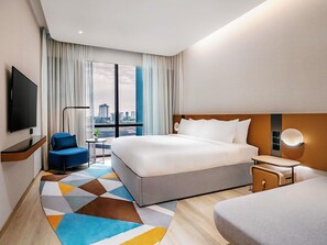 A hotel room with a large bed, a TV, a desk, a chair, and a view of the cityscape. - Novotel Johor Bahru City Centre (Johor Bahru)