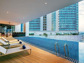 Una piscina infinita con sillones de descanso y vistas a un edificio moderno.