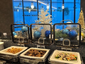 Buffet-style food service with various dishes, including meat, vegetables, and desserts, in a commercial setting with a view of the outside. - Novotel Johor Bahru City Centre (Johor Bahru)