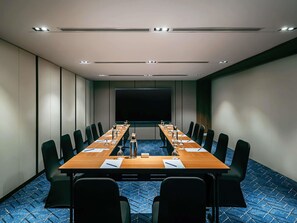 A conference room with a long table, black chairs, a projector screen, and a blue patterned carpet. - Novotel Johor Bahru City Centre (Johor Bahru)