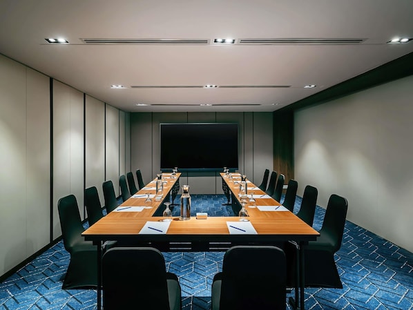 A conference room with a long table, black chairs, a projector screen, and a blue patterned carpet. - Novotel Johor Bahru City Centre (Johor Bahru)