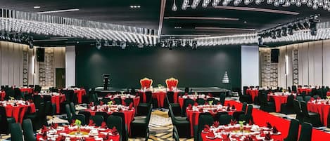 Un salón de banquetes con filas de mesas, un escenario y una araña.
