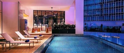 A modern indoor pool area with lounge chairs and a view of a high-rise building.