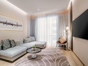 A modern living room with a sectional sofa, a coffee table, a floor lamp, and a large TV. - Novotel Johor Bahru City Centre (Johor Bahru)