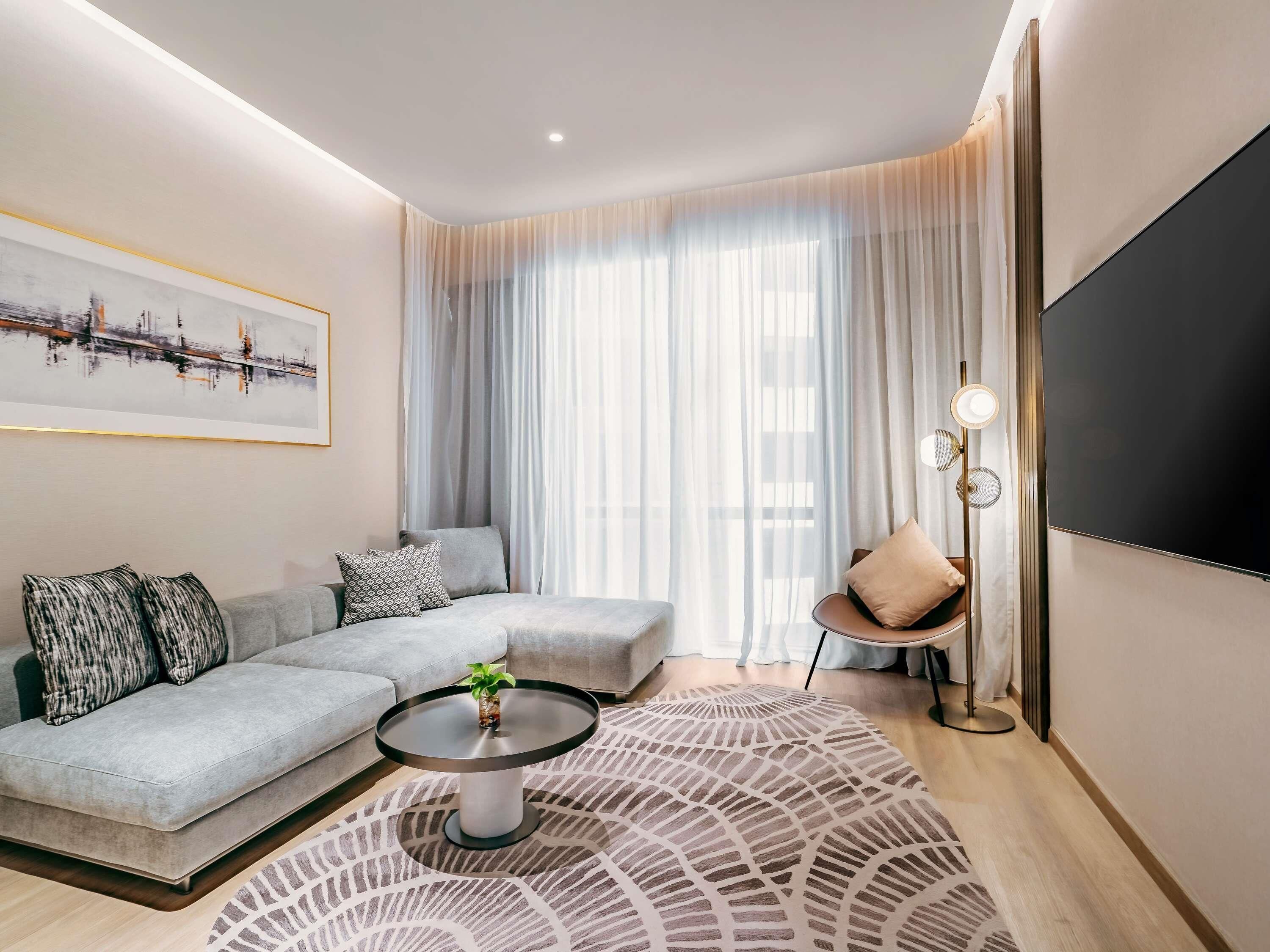 A modern living room with a sectional sofa, a coffee table, a floor lamp, and a large TV.