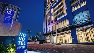 A hotel entrance with illuminated signage, a paved walkway, and a cityscape in the background.