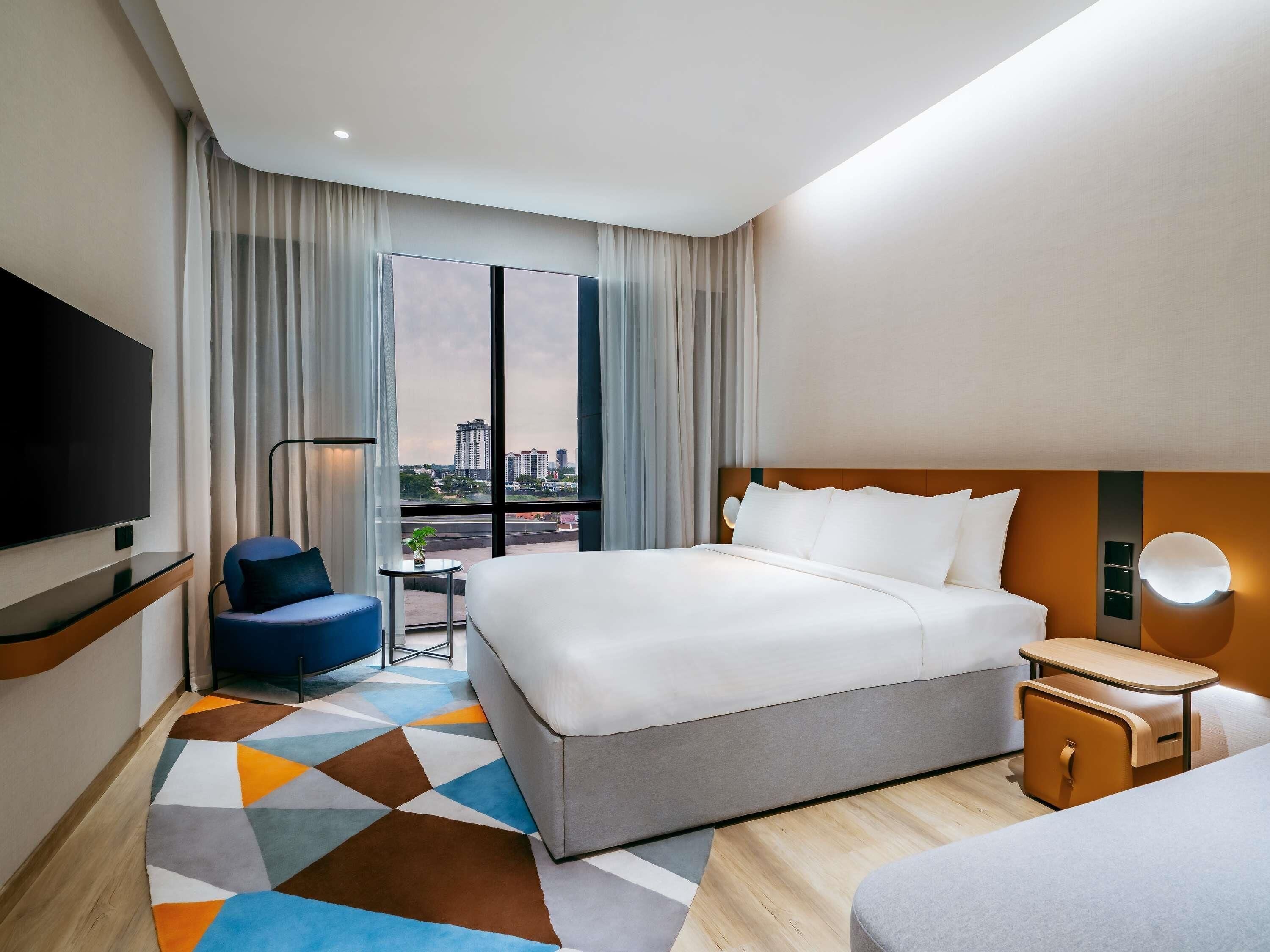 Habitación de hotel con una cama grande, televisión, escritorio y vistas de la ciudad.