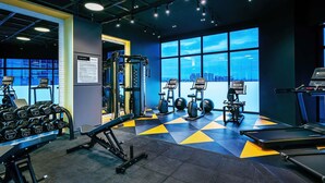Un gimnasio con equipo de ejercicio, cintas de correr y vistas a la ciudad a través de amplias ventanas.