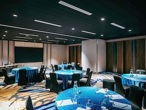 A conference room with round tables, chairs, and a large screen. - Novotel Johor Bahru City Centre (Johor Bahru)