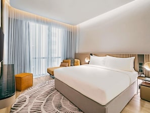 A modern hotel room with a large bed, a bedside table, a lamp, and a view of the city through sheer curtains. - Novotel Johor Bahru City Centre (Johor Bahru)