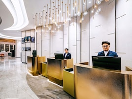 A modern hotel reception area with a curved marble floor, gold reception desks, and a wall-mounted display of framed pictures.