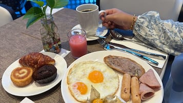 Une table mise pour le petit-déjeuner, avec des assiettes remplies de nourriture, une tasse de café, un verre de jus de fruits et une plante.