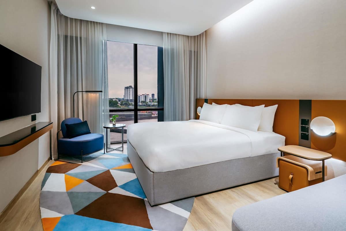 A hotel room with a large bed, a TV, a desk, and a view of the city.