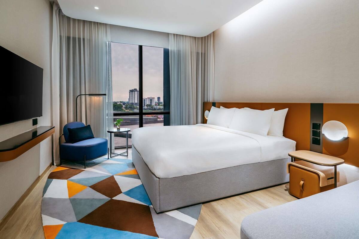 A hotel room with a large bed, a TV, a desk, and a view of the city.