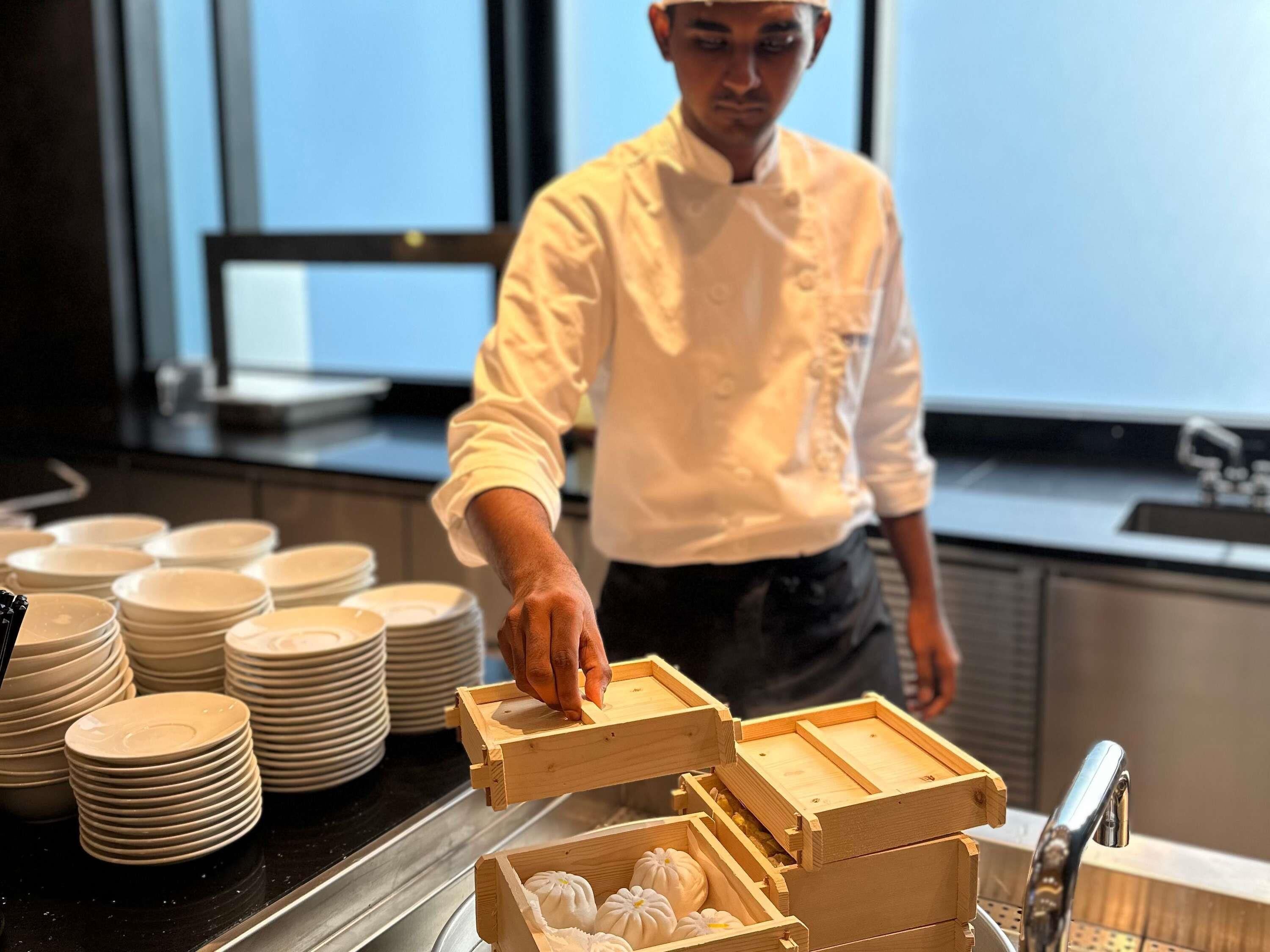 A chef in a white uniform arranging wooden food containers in a kitchen with a modern design.