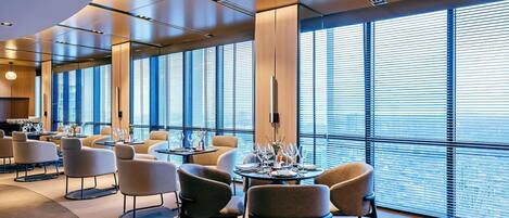 A modern hotel dining area with large windows, contemporary furniture, and a clean, well-lit interior.