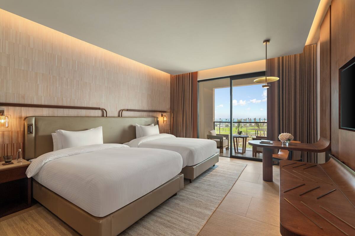 Habitación de hotel con dos camas, un ventanal con vistas, zona de comedor y televisión.