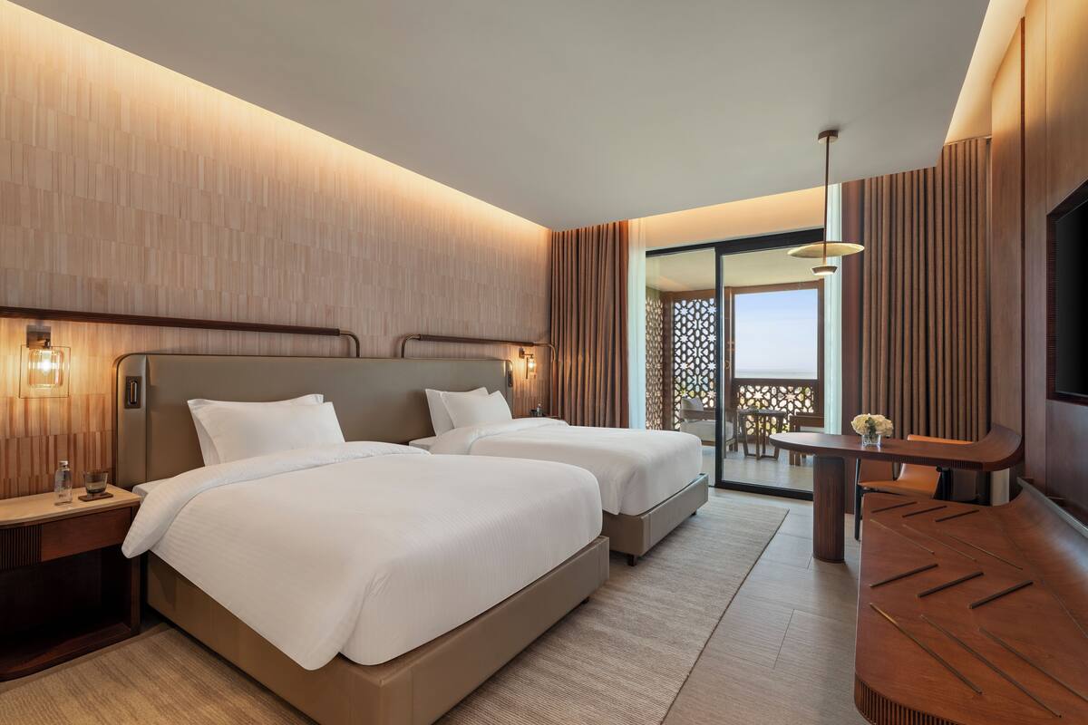 Una habitación de hotel moderna con dos camas, un escritorio y un balcón con vistas.