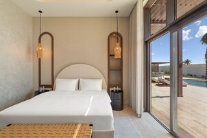 Habitación de hotel moderna con una cama grande, dos lámparas colgantes, una mesita de noche y vistas a una zona de piscina al aire libre.