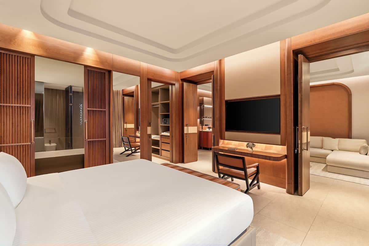 Una habitación de hotel moderna con una cama grande, un escritorio con una silla, un televisor, un sofá y un vestidor.