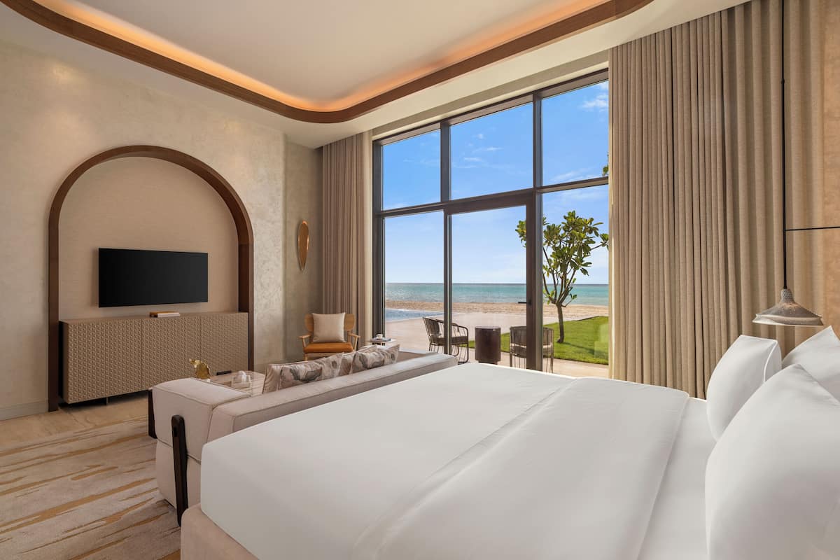 Habitación de hotel con una cama grande, televisión, zona de estar y vistas a la playa.