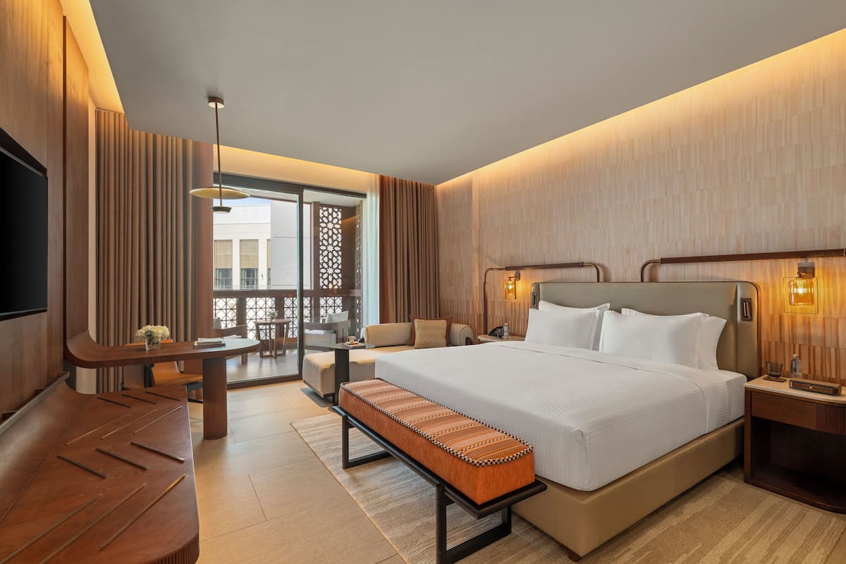 Una habitación de hotel moderna con una cama grande, un banco, un escritorio y un balcón con vistas.