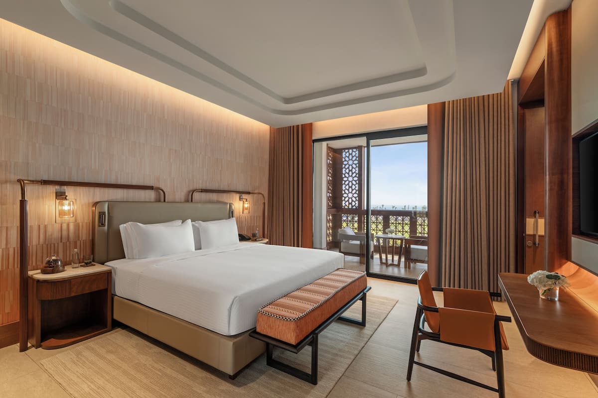 Habitación de hotel moderna con una cama grande, mesitas de noche, un escritorio y un balcón con vistas.