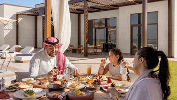 Una mesa de comedor con diversos platos y bebidas, ubicada al aire libre con un edificio moderno al fondo.